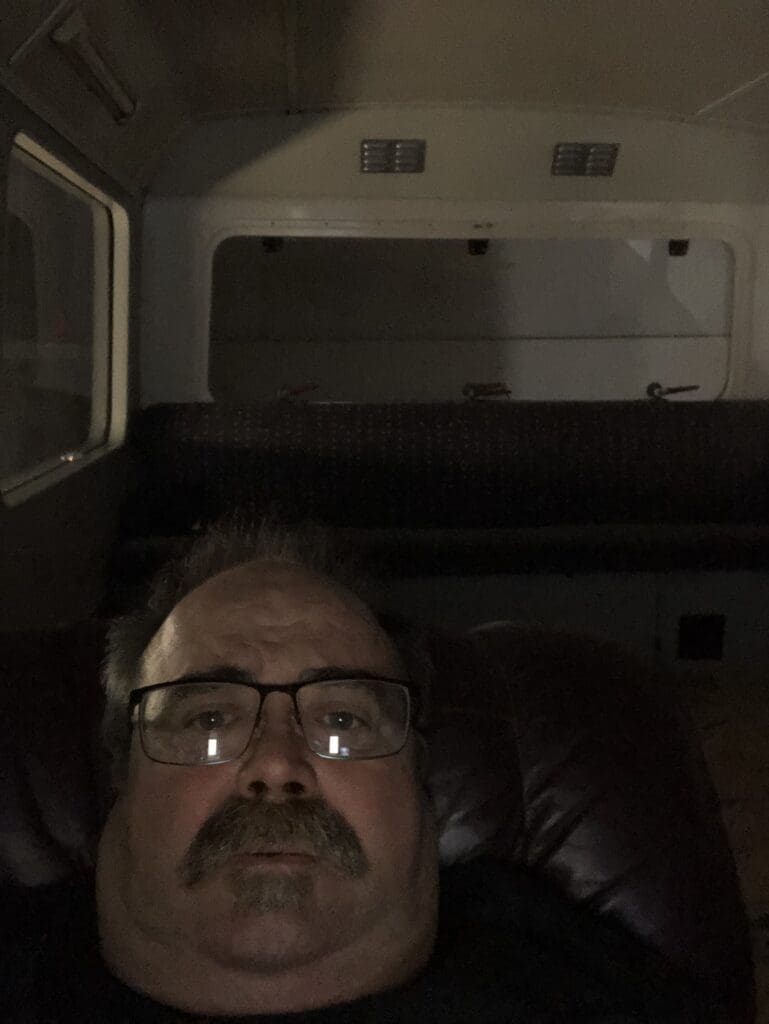 A man with glasses is sitting in the dark.